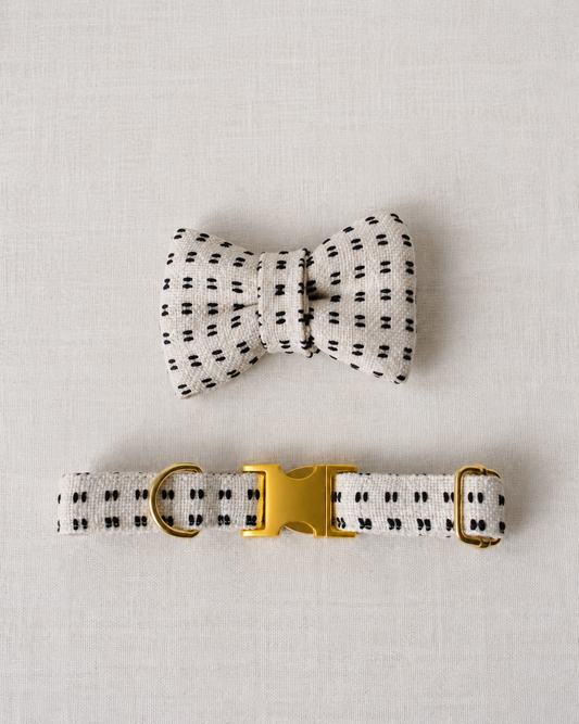 A matching pet accessory set featuring a small bow tie and a collar, both made from a textured off-white fabric with a small black dotted pattern, complete with a shiny gold buckle.