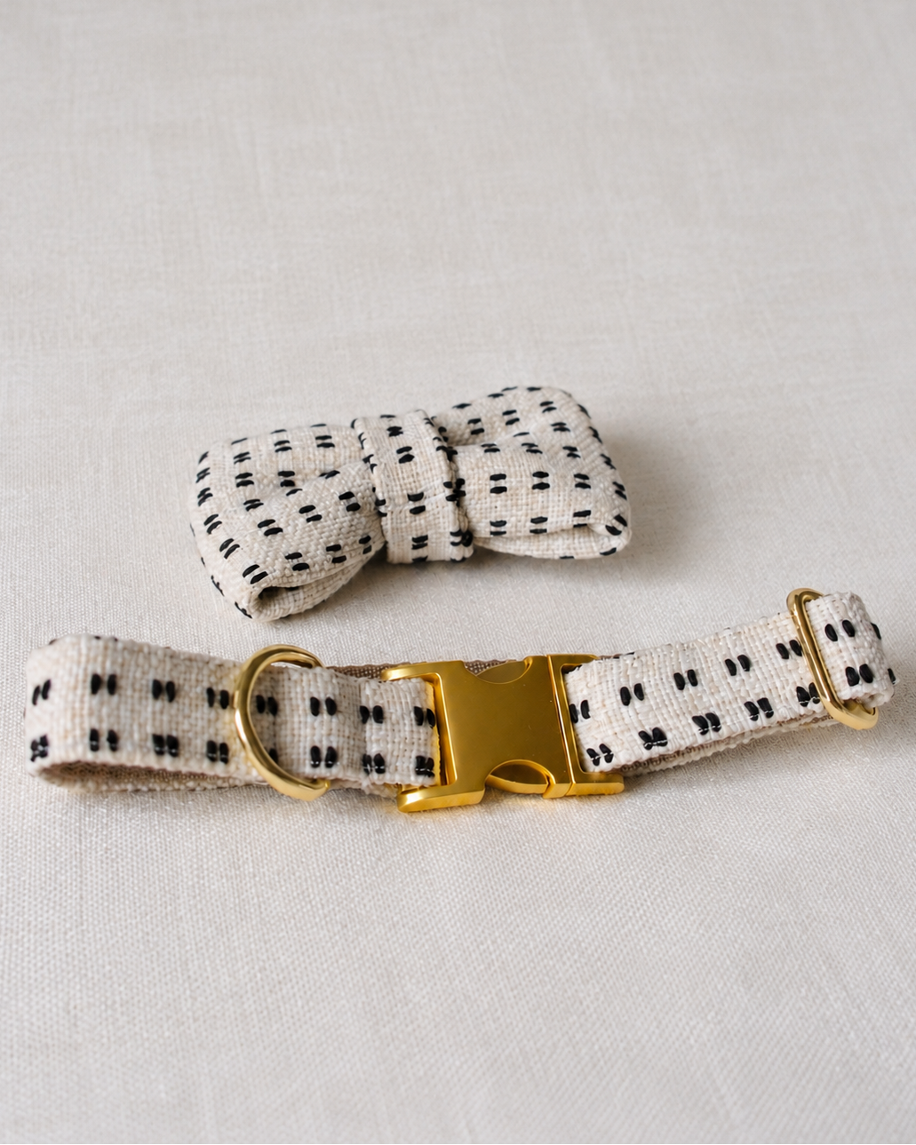 A matching pet collar and bow tie set made from a cream-colored fabric with a small black dotted pattern, featuring a gold-tone metal buckle and hardware.