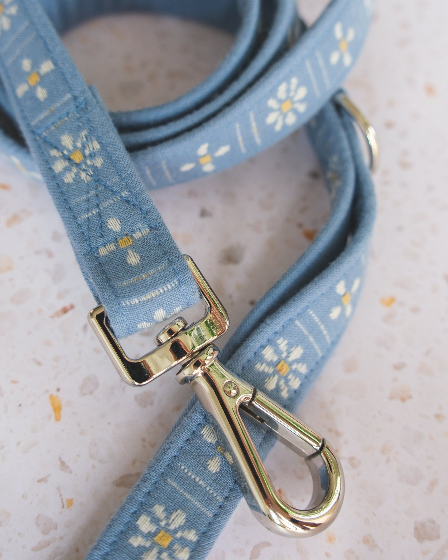 Blue floral-patterned dog leash with a gold clasp on a light background
