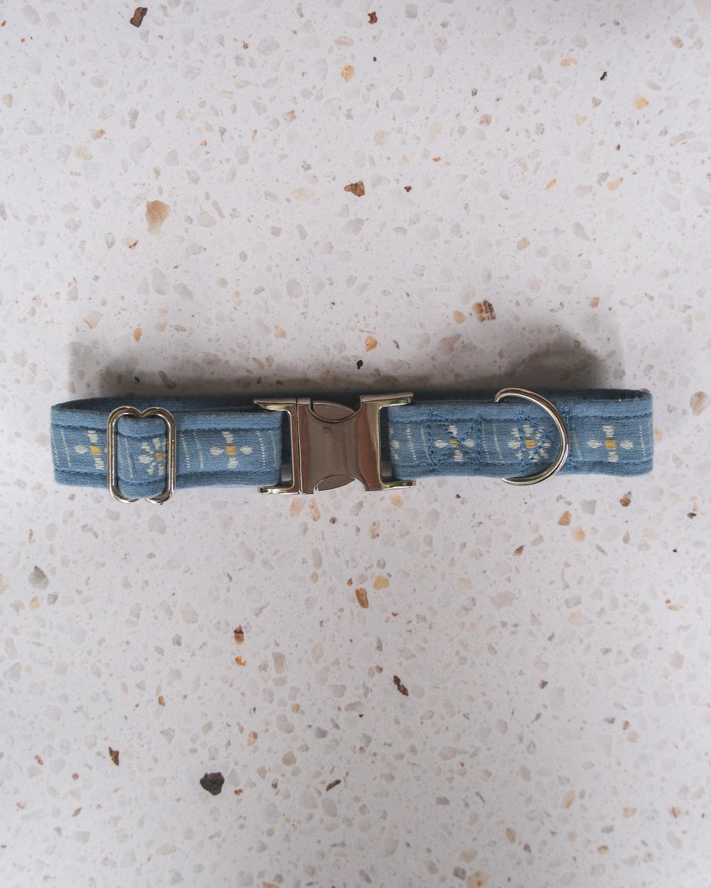 Blue flower dog collar with metal buckle on a speckled gray surface